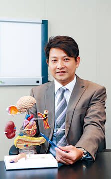 張偉成醫生身穿西裝與人體解剖模型合影